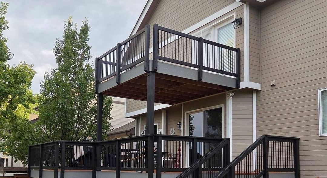 Two story deck with black railing and stairs, built by New West Co against a black background.